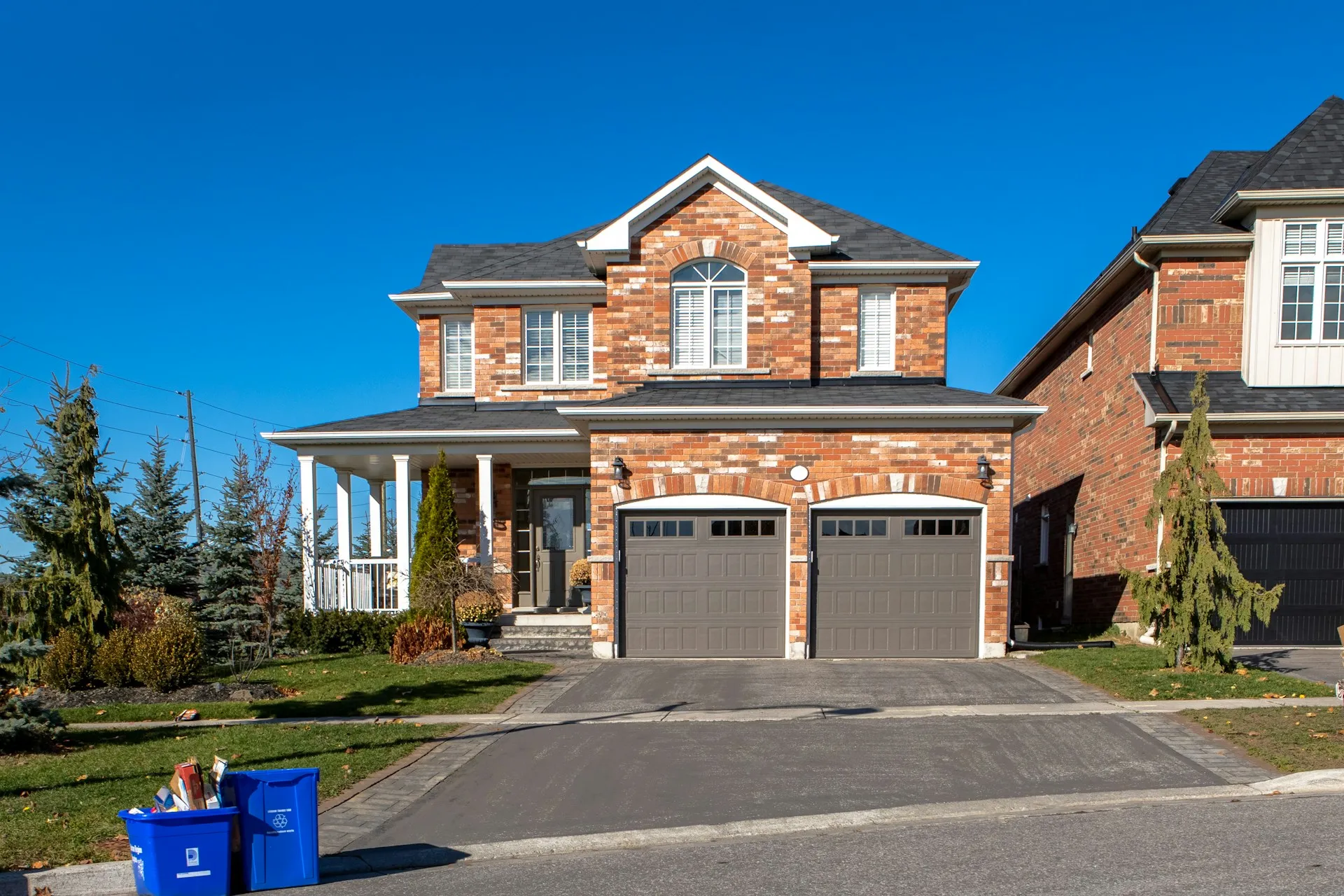 Red brick two-storey home with two brown carriage-style garage doors